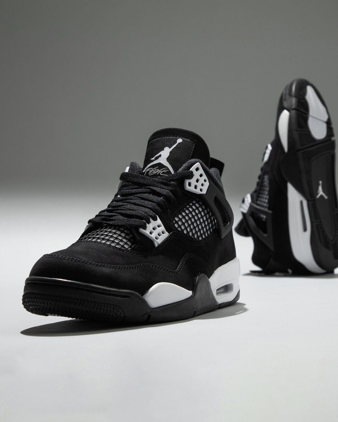 Air Jordan 4 "White Thunder" sneakers, featuring a sleek black nubuck upper contrasted by crisp white mesh accents